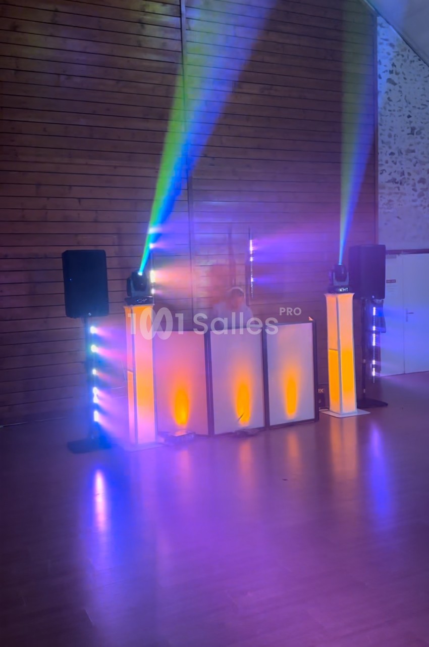 Un DJ mixe derrière une table éclairée par des lumières colorées dans une salle aux murs en bois.