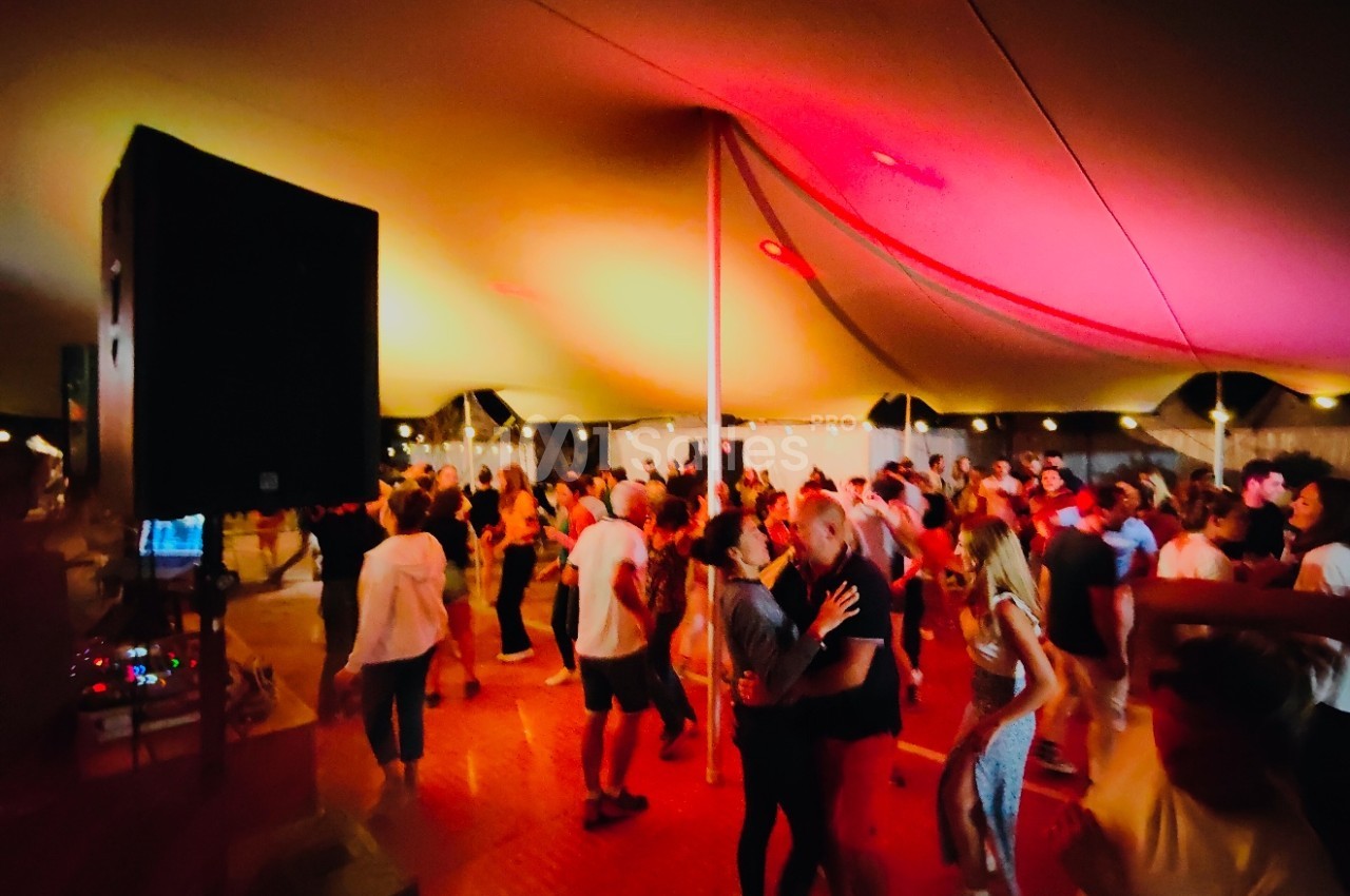 Des personnes dansent sous une grande tente éclairée de lumières colorées lors d'un événement festif en soirée.