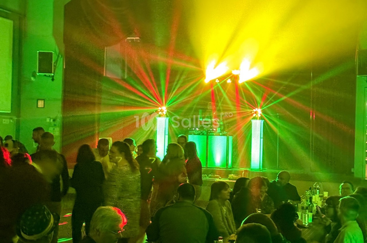 Des personnes dansent dans une salle éclairée par des jeux de lumière colorés provenant d'une scène avec un DJ.