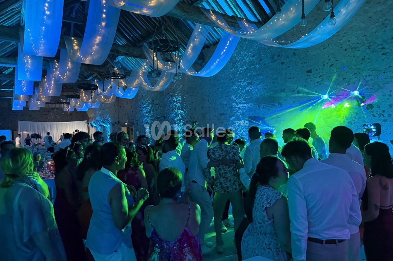 Groupe de personnes dans une salle en pierre éclairée par des lumières colorées, lors d'une fête ou d'un événement.