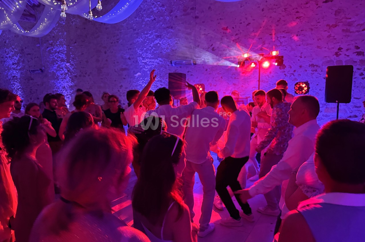 Groupe de personnes dansant sous des lumières colorées dans une salle en pierre décorée de voilages et guirlandes lumineuses.