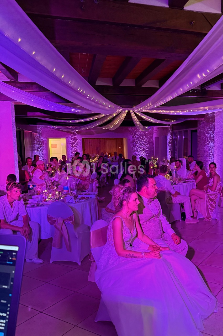 Des invités assis dans une salle de réception décorée de voilages et lumières violettes, lors d’un mariage.