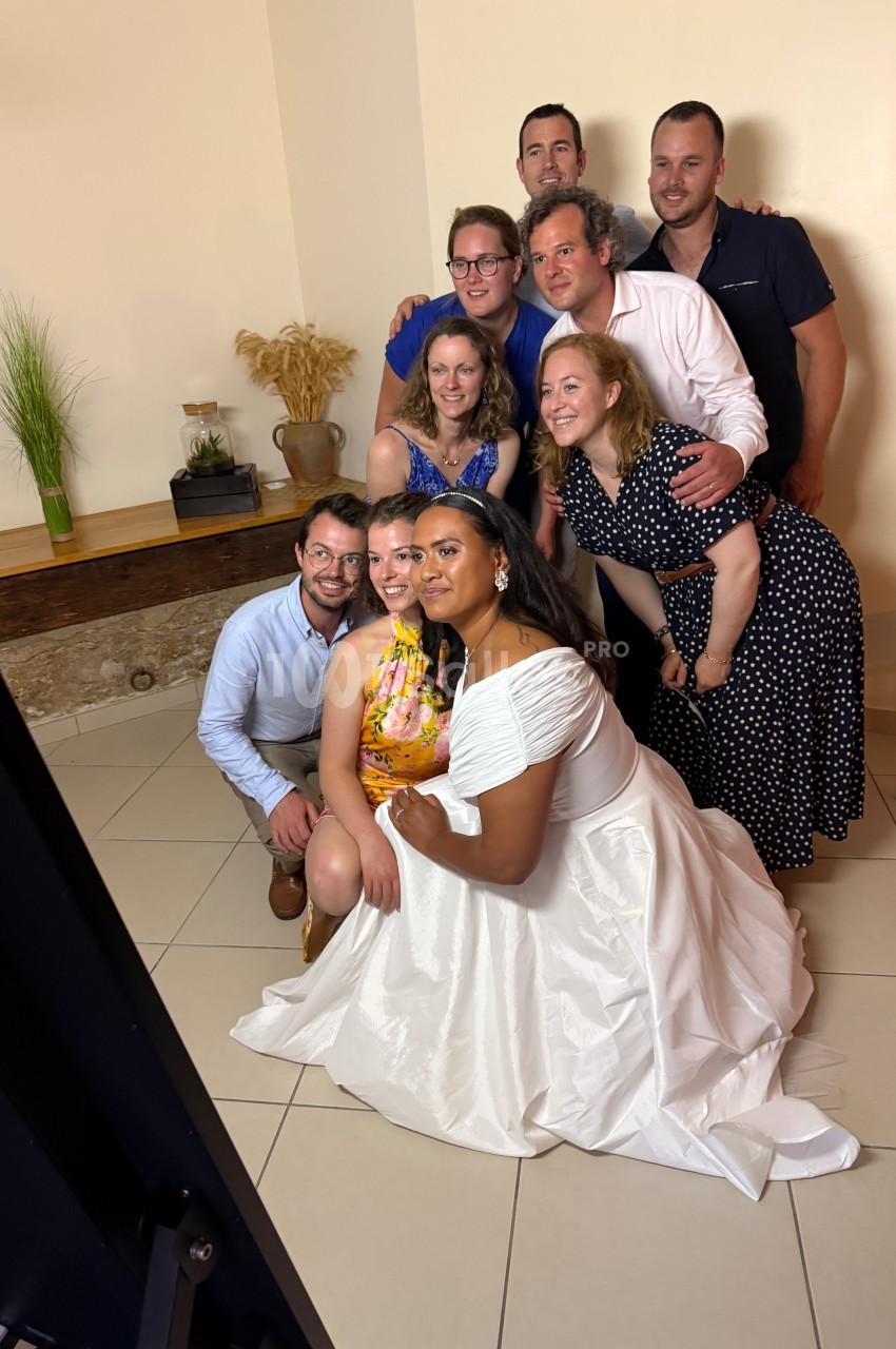 Un groupe de personnes posant ensemble dans une pièce lumineuse, avec une femme en robe blanche au premier plan.