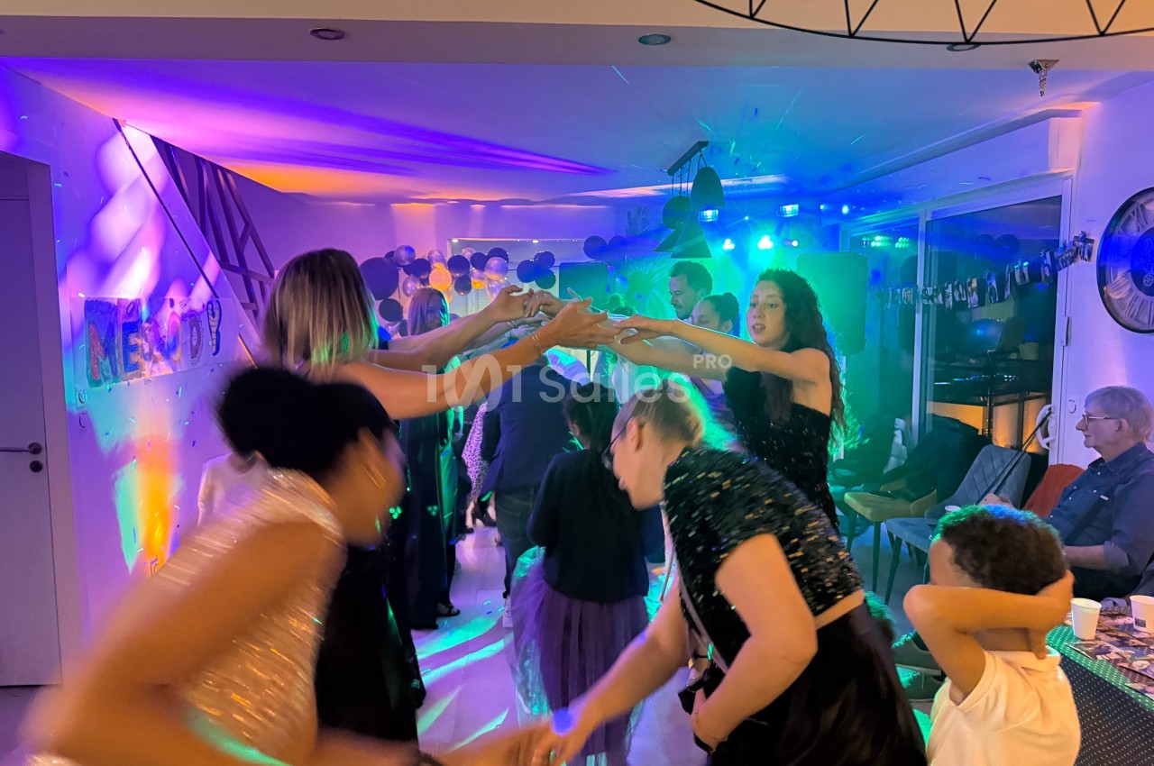 Des personnes dansent sous des lumières colorées lors d'une fête dans une salle décorée.
