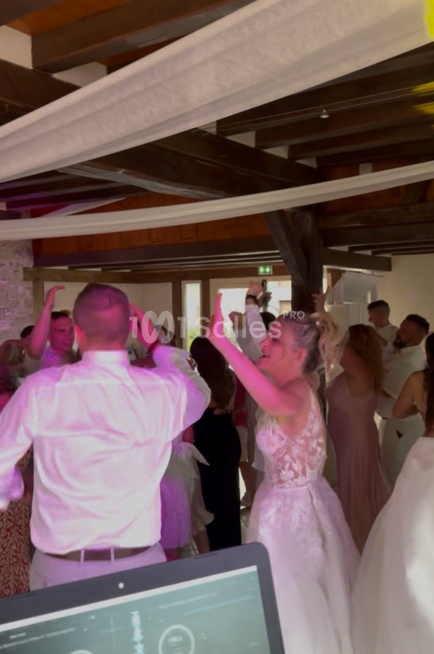 Des invités dansent joyeusement lors d'une réception de mariage dans une salle en bois avec éclairage coloré.
