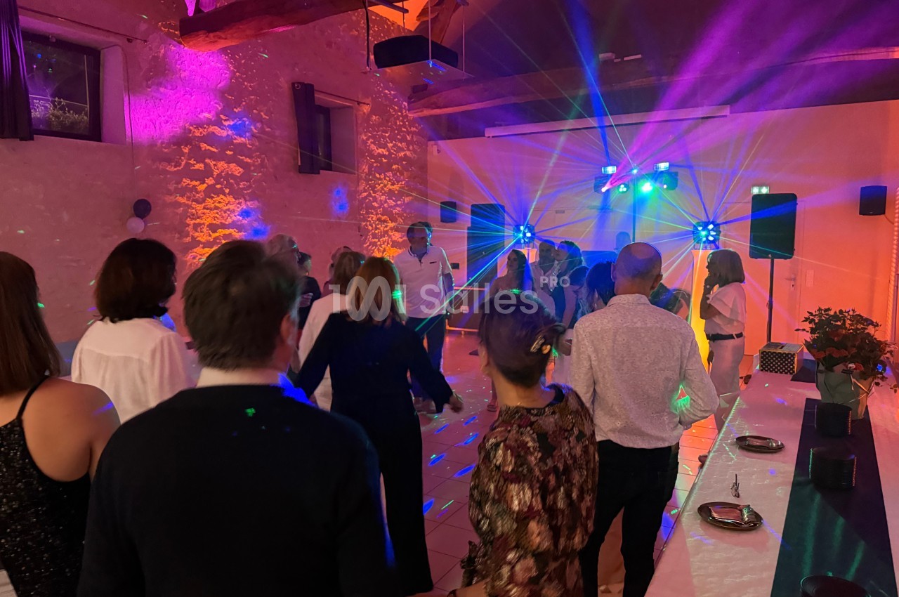 Des personnes dansent sous des jeux de lumière colorés dans une salle aux murs en pierre.