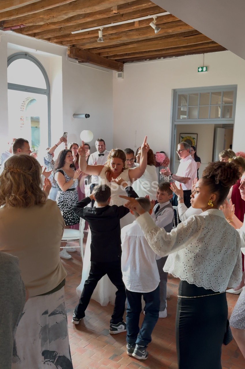 Des personnes dansent joyeusement dans une salle lumineuse avec des murs blancs et de grandes fenêtres.