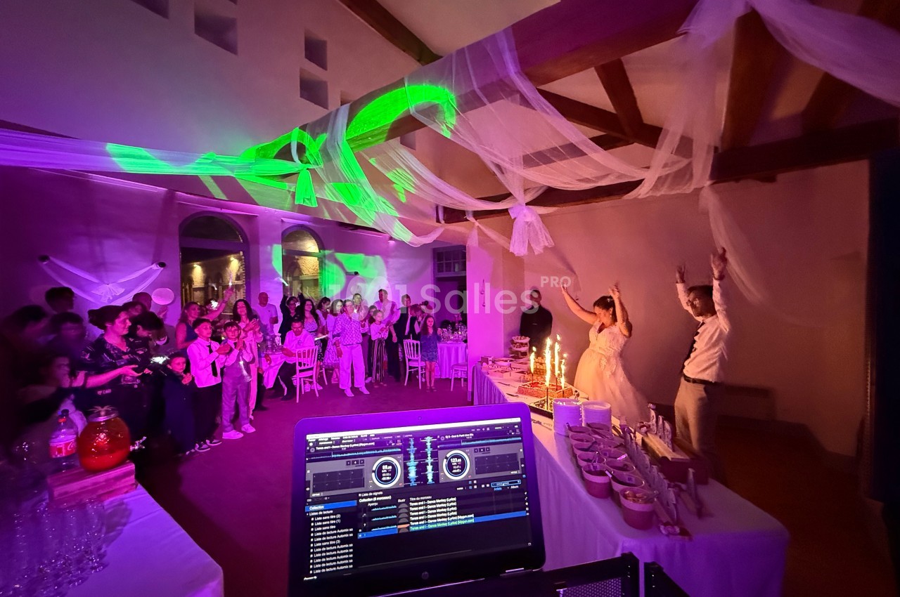 Salle de réception décorée, ambiance festive avec des invités, un couple célébrant et une table de buffet éclairée.