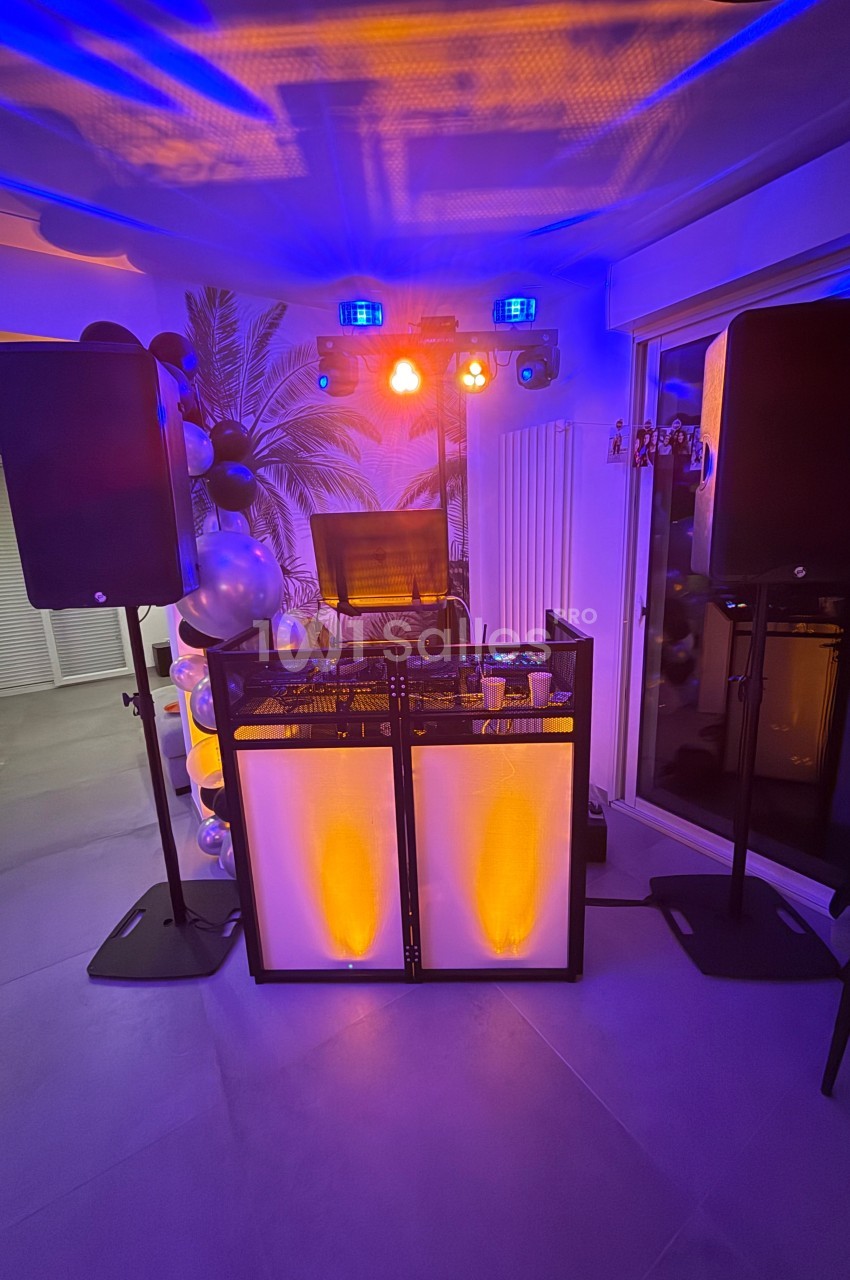 Installation de matériel de DJ avec lumières colorées, enceintes et table de mixage dans une pièce décorée.