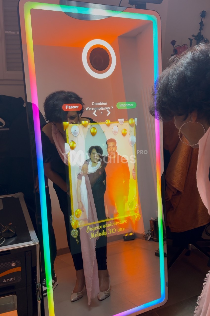 Une femme interagit avec un miroir photobooth lumineux affichant une photo personnalisée d'anniversaire.