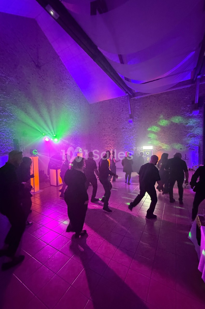 Personnes dansant dans une salle éclairée par des lumières colorées, avec un mur en pierre en arrière-plan.