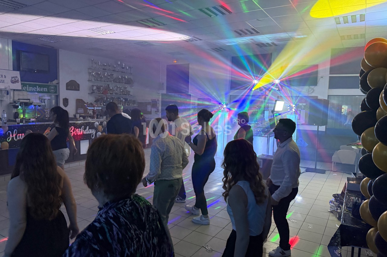 Personnes dansant dans une salle éclairée par des jeux de lumière colorés, avec des décorations et un bar en arrière-plan.