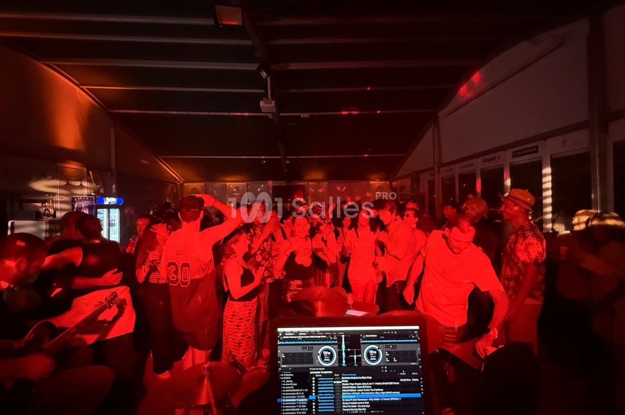 Groupe de personnes dansant dans une ambiance festive et lumineuse avec un DJ en arrière-plan.