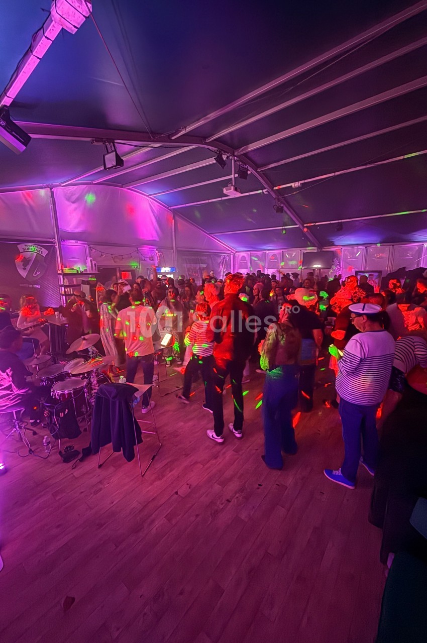 Des personnes dansent sous des lumières colorées dans une salle avec un groupe de musique jouant sur scène.