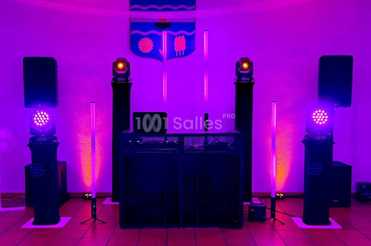 Installation de matériel de sonorisation et éclairage coloré dans une salle avec un blason au mur.
