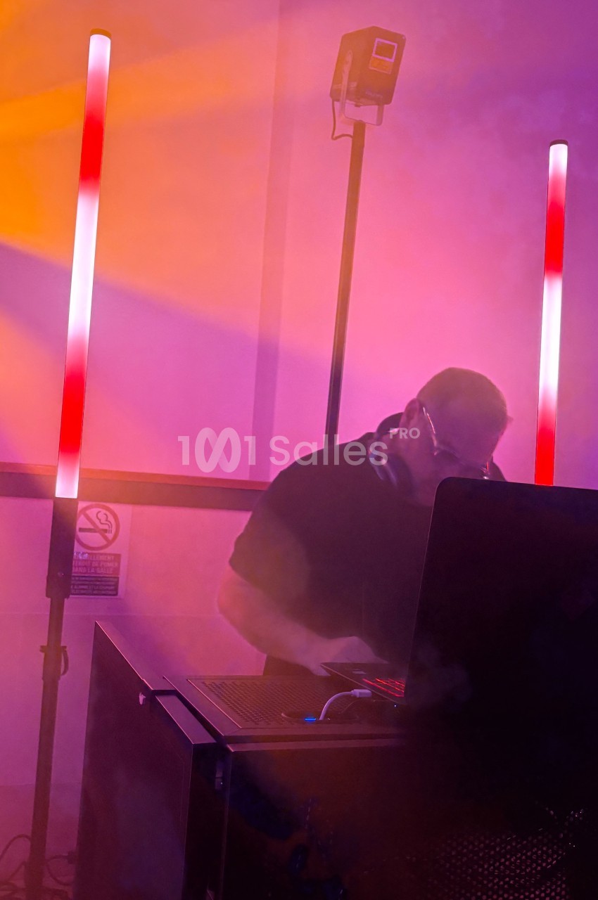 Un DJ mixant sur son ordinateur portable, entouré de lumières colorées et d'une ambiance enfumée.