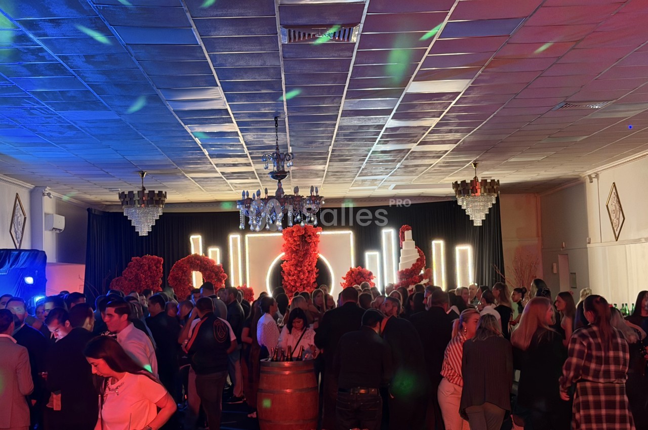 Soirée dans une salle aux éclairages bleus et rouges, convives debout devant un décor de fleurs rouges et lumières vives.