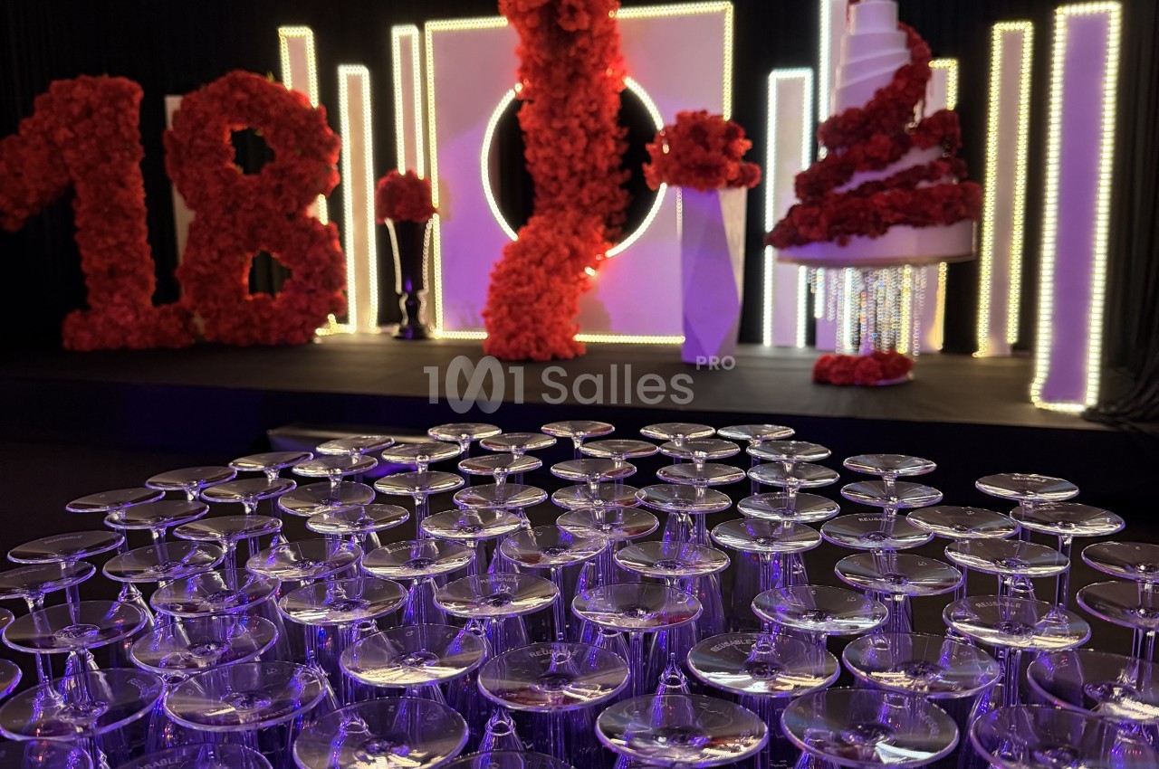 Coupes alignées au premier plan, devant une scène décorée de chiffres floraux rouges et de panneaux lumineux violets.