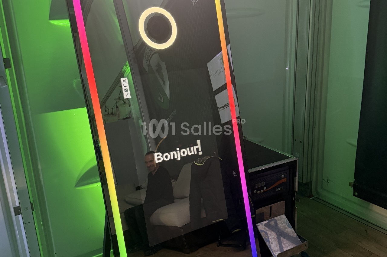 Miroir photo lumineux à bordure LED multicolore, avec écran affichant « Bonjour » et un anneau lumineux, installé dans un espace à éclairage vert. Wait, I must not transcribe text incrusted in the image (the "Bonjour!" is on-screen text, and "1001