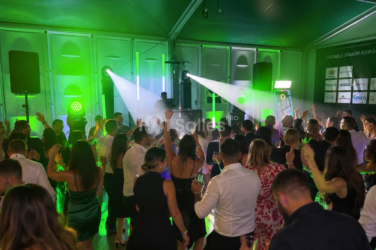 Soirée dansante sous chapiteau éclairé en vert, avec une foule de convives les bras levés devant un DJ et des projecteurs à faisceaux blancs.