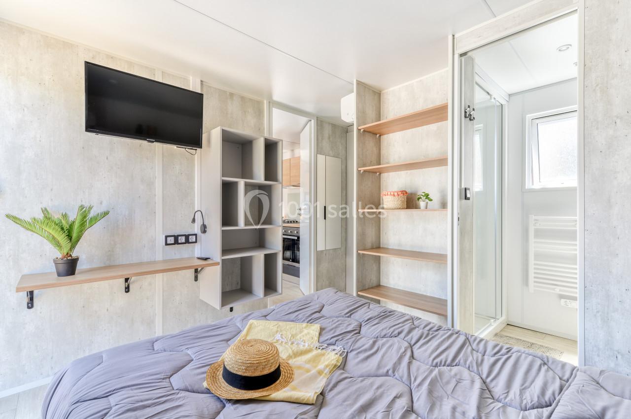 Chambre lumineuse avec lit, étagères, télévision murale, et accès à une salle de bain moderne.