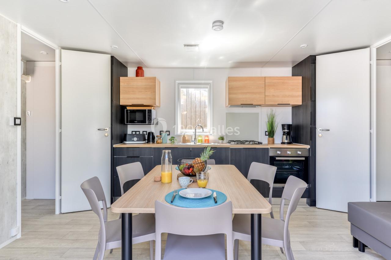 Cuisine moderne avec table à manger dressée, chaises grises, et meubles en bois clair dans un espace lumineux.
