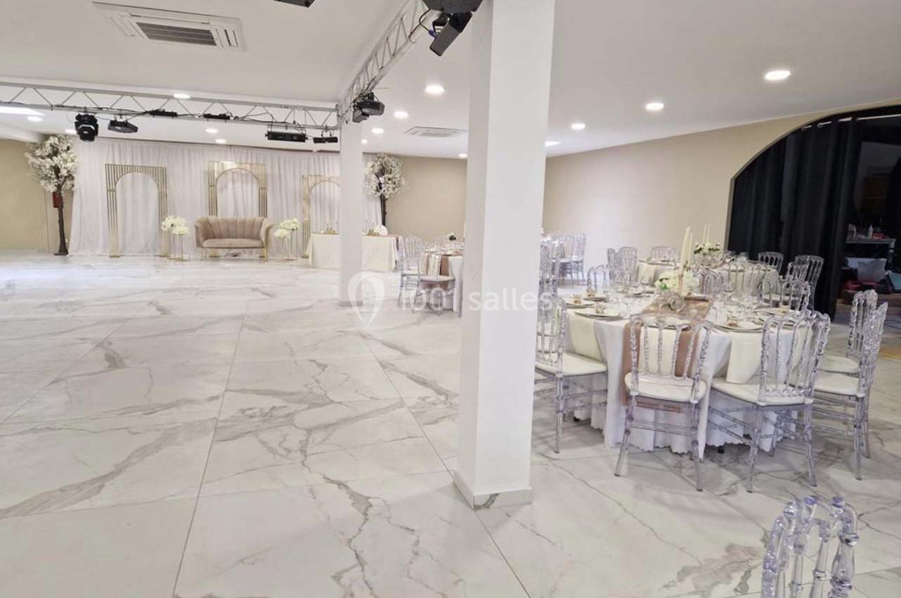 Salle de réception lumineuse avec tables dressées, chaises transparentes et décoration florale élégante.