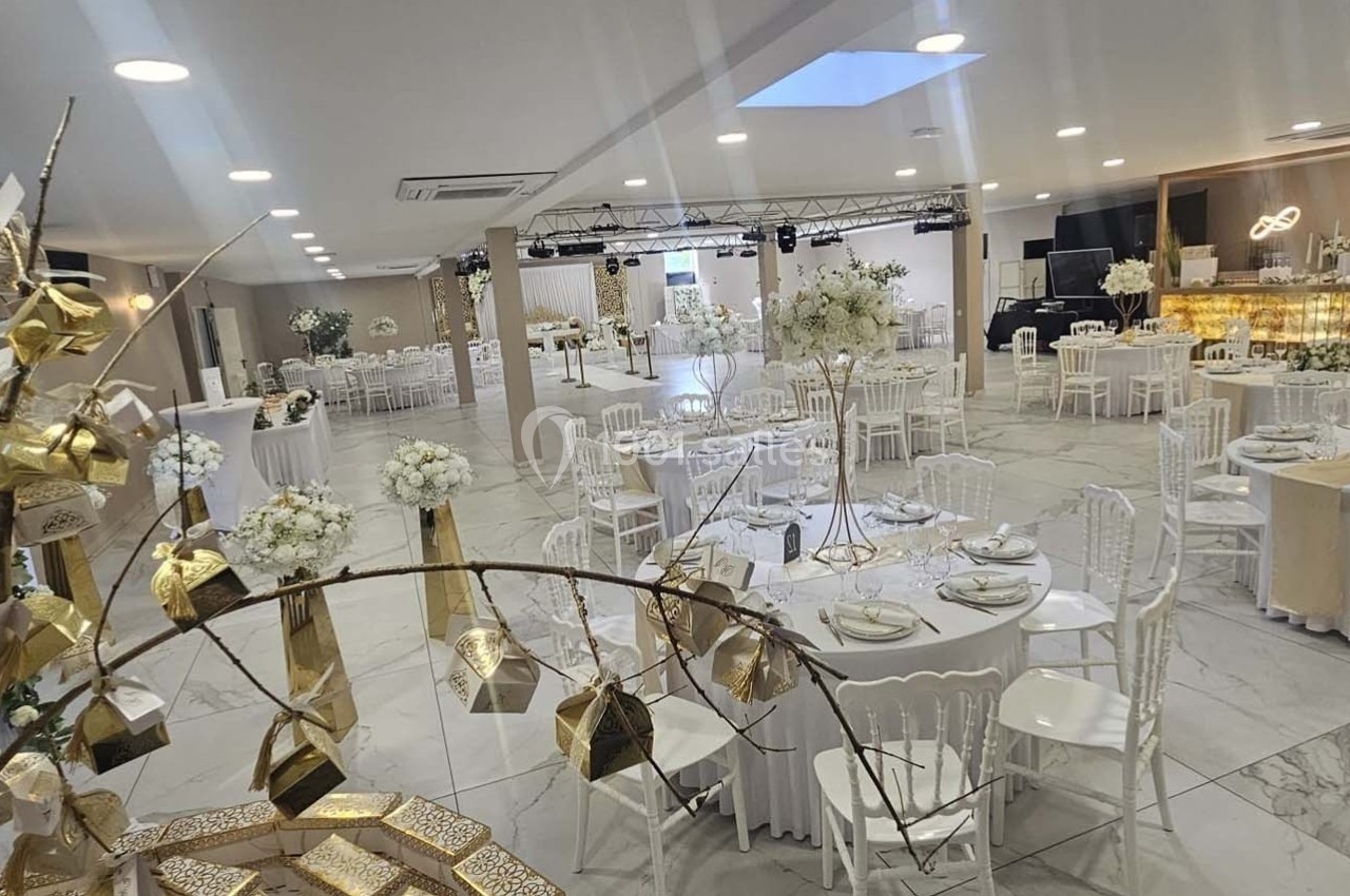 Salle de réception élégante avec tables rondes décorées de blanc et doré, et un espace pour la scène au fond.