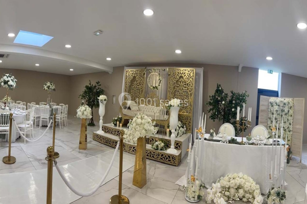 Salle de réception décorée avec des fleurs blanches, des tables dressées et une scène ornée de motifs dorés.