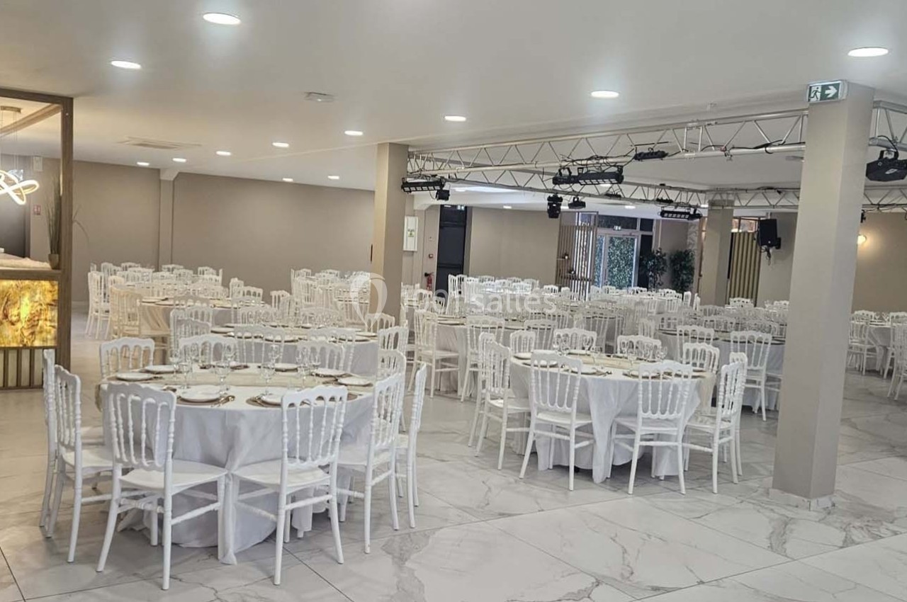 Salle de réception lumineuse avec tables rondes dressées, chaises blanches et décorations sobres.