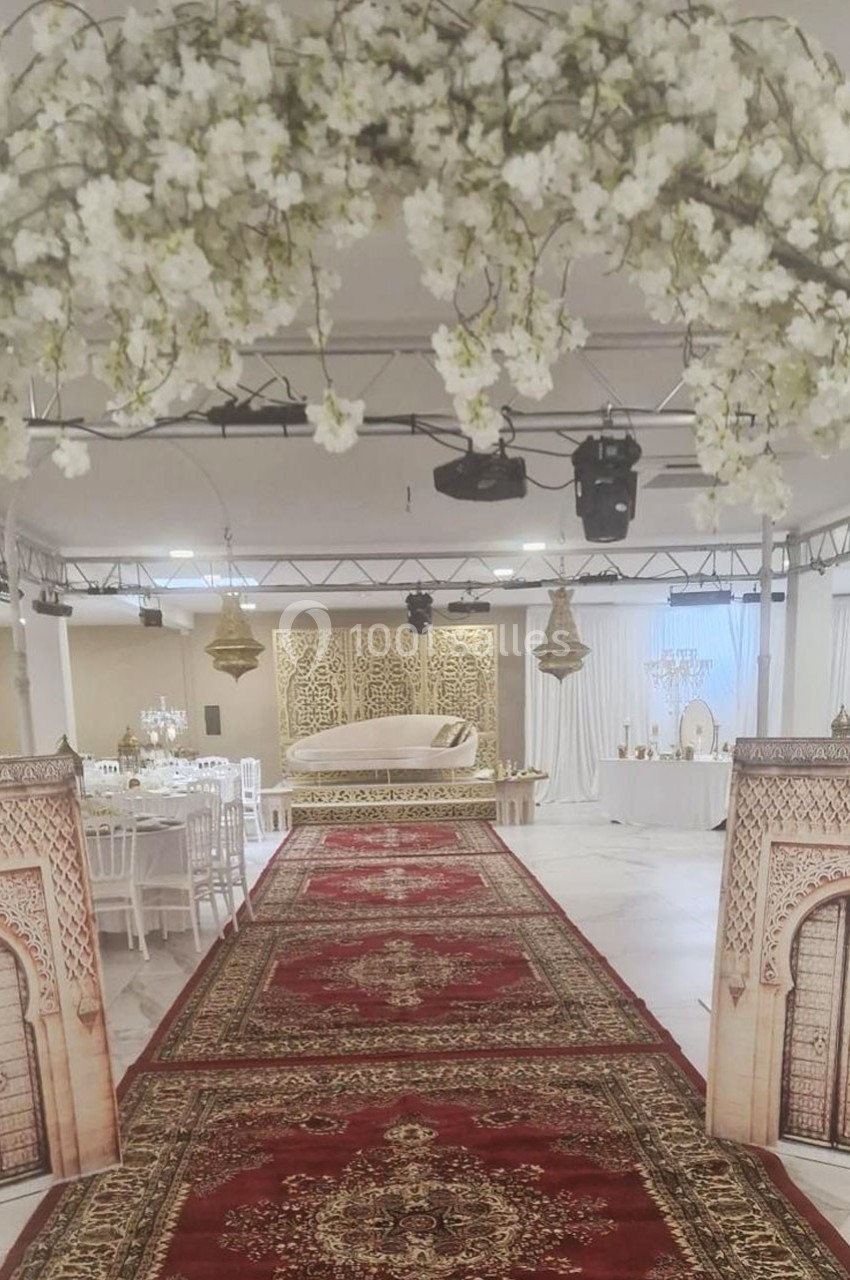 Décoration de salle de réception avec arche florale, tapis rouges ornés et estrade ornée de motifs dorés.