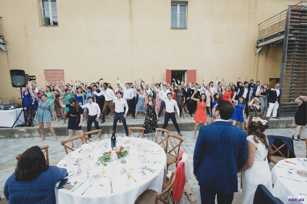 Des invités dansent en groupe lors d'une réception de mariage en extérieur devant un bâtiment beige.