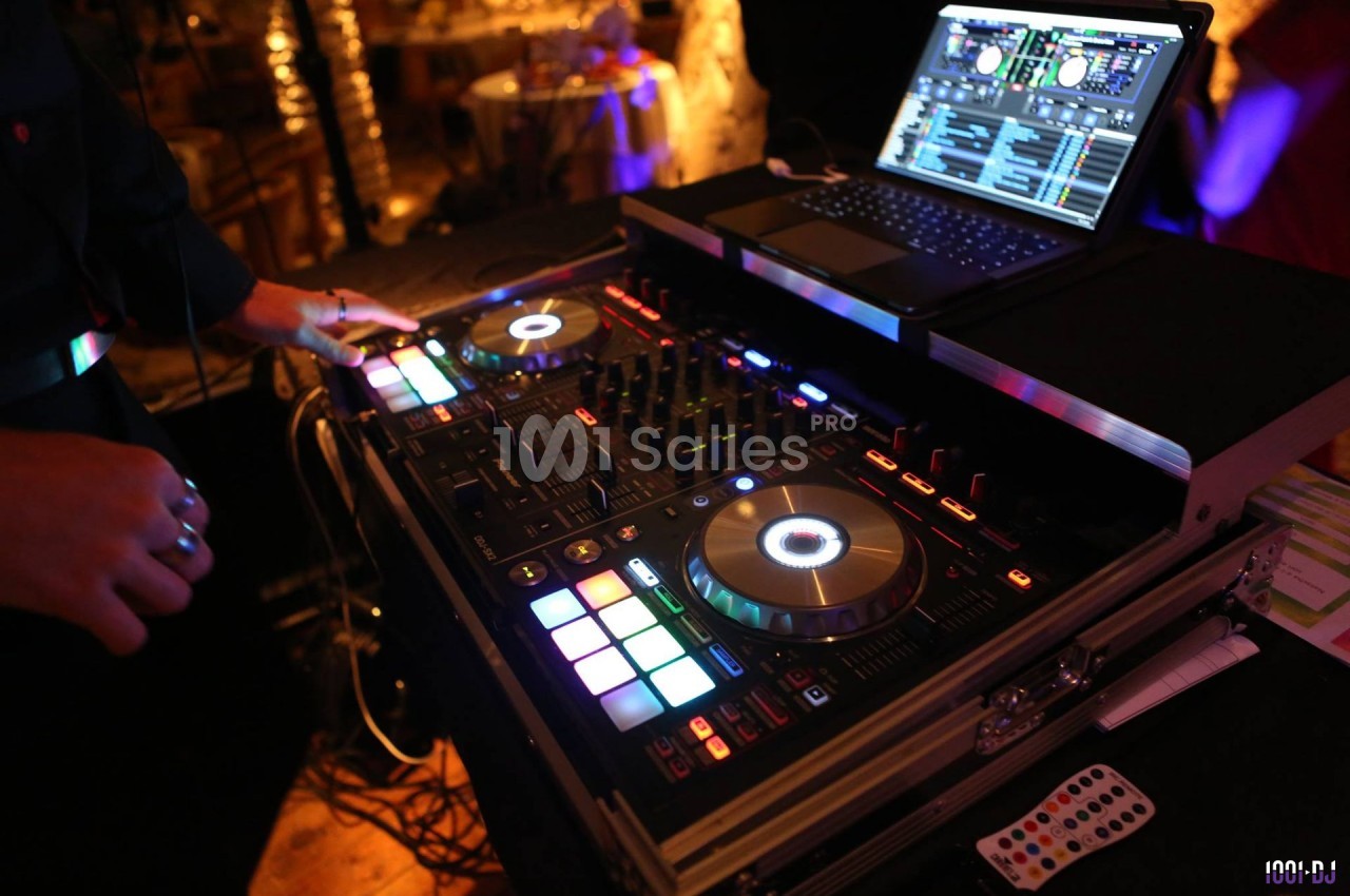 Un DJ manipule une table de mixage lumineuse avec un ordinateur portable ouvert à proximité.