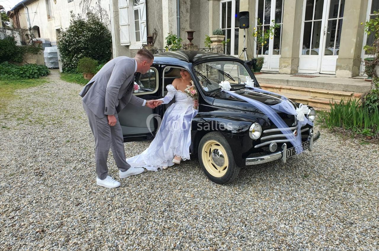 MARIES DEVANT LE CHATEAU Un marié aide sa partenaire en robe de mariée à sortir d'une voiture ancienne décorée pour un mariage.