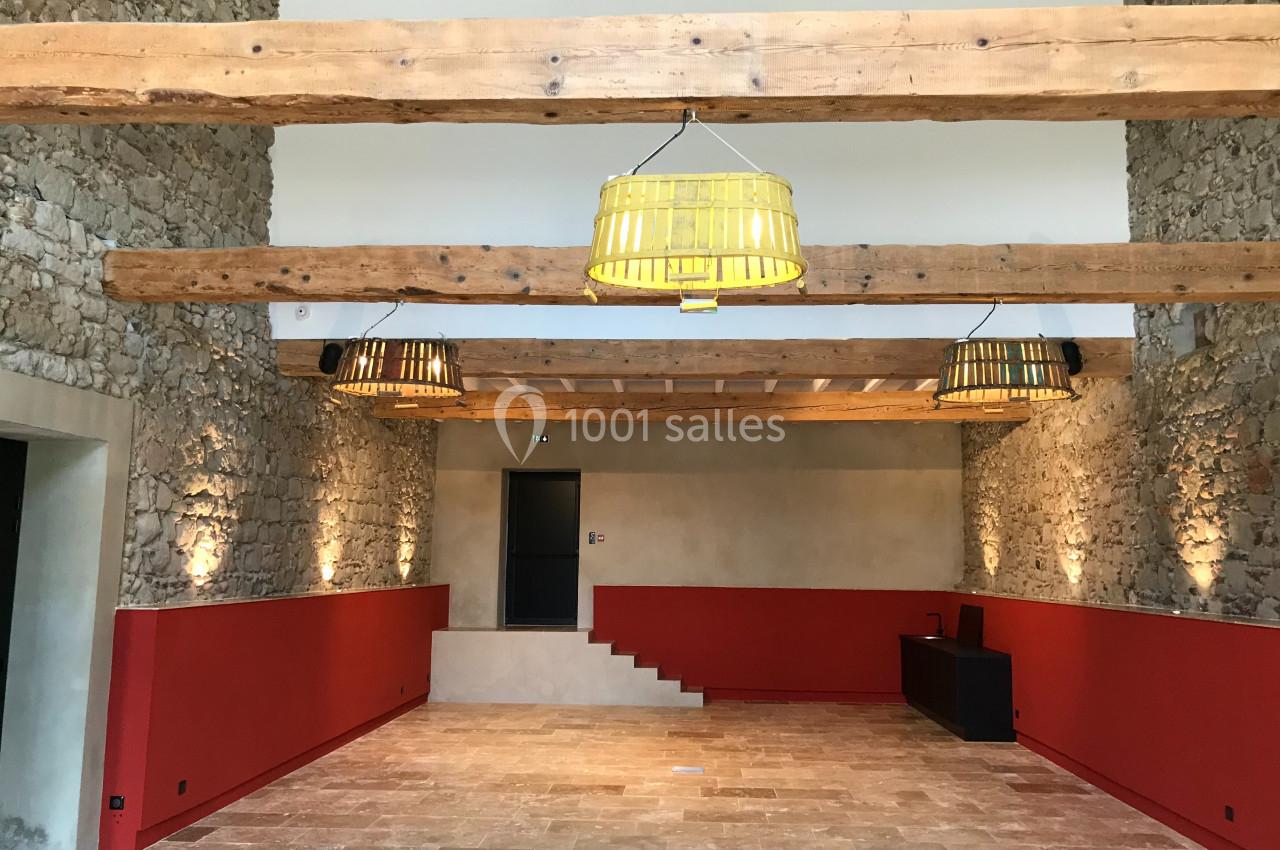 SALLE COVENTIS Salle intérieure avec murs en pierre, poutres apparentes, suspensions jaunes et rouges, et sol en pierre beige.