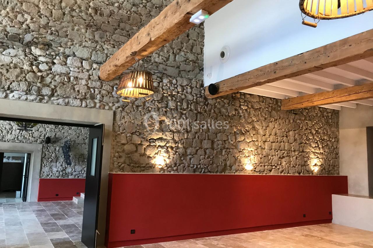 SALLE COVENTIS Salle avec murs en pierre apparente, poutres en bois au plafond, sol en pierre et éclairage suspendu.