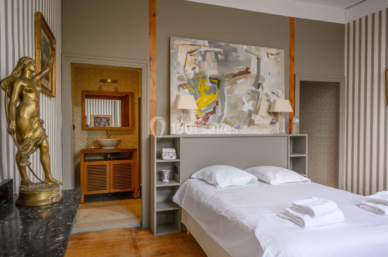 Chambre avec lit double, décoration artistique, statue dorée, et vue sur une salle de bain attenante avec vasque.
