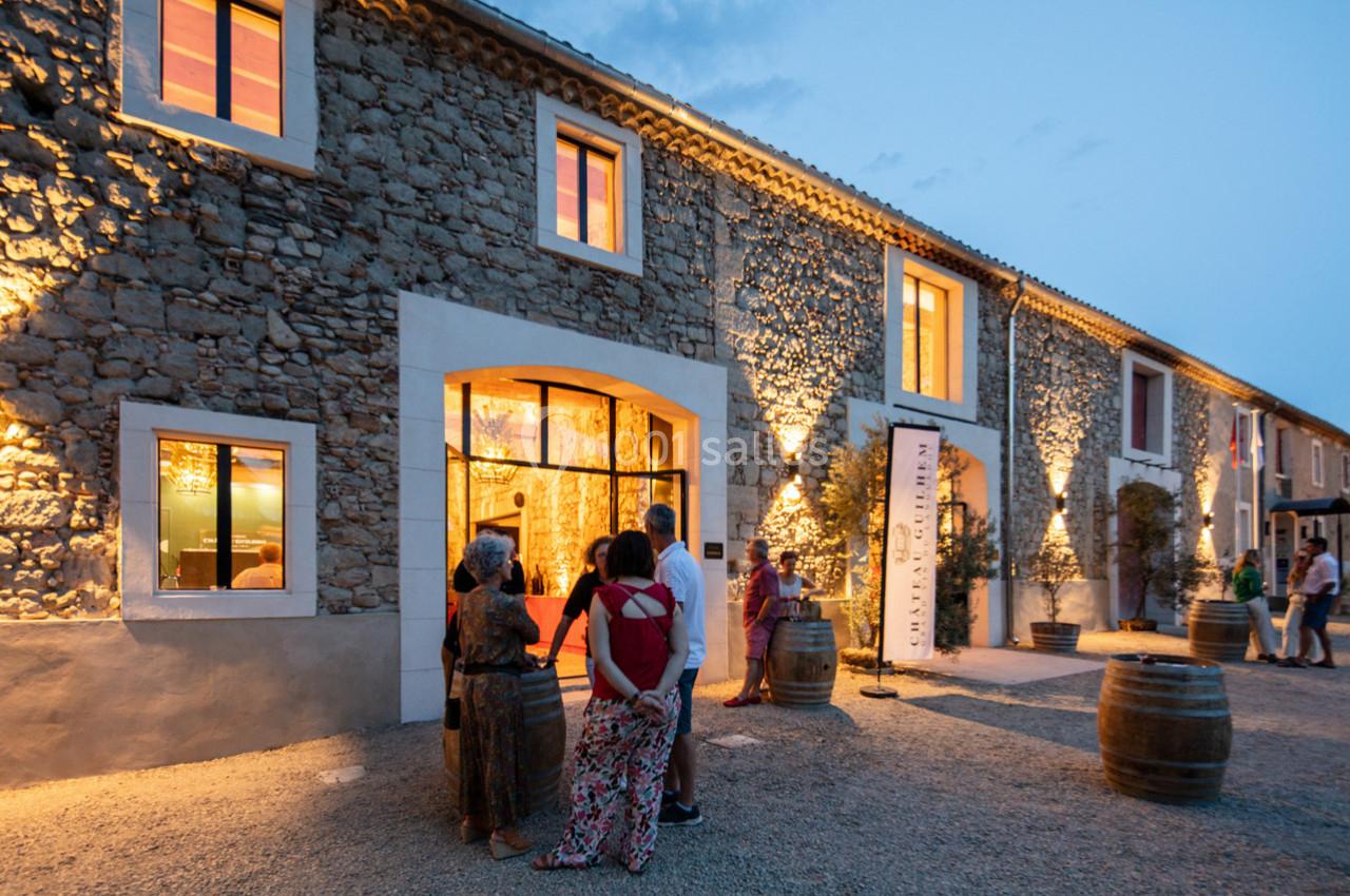 Façade en pierre éclairée d'un bâtiment avec des visiteurs rassemblés devant l'entrée au crépuscule.