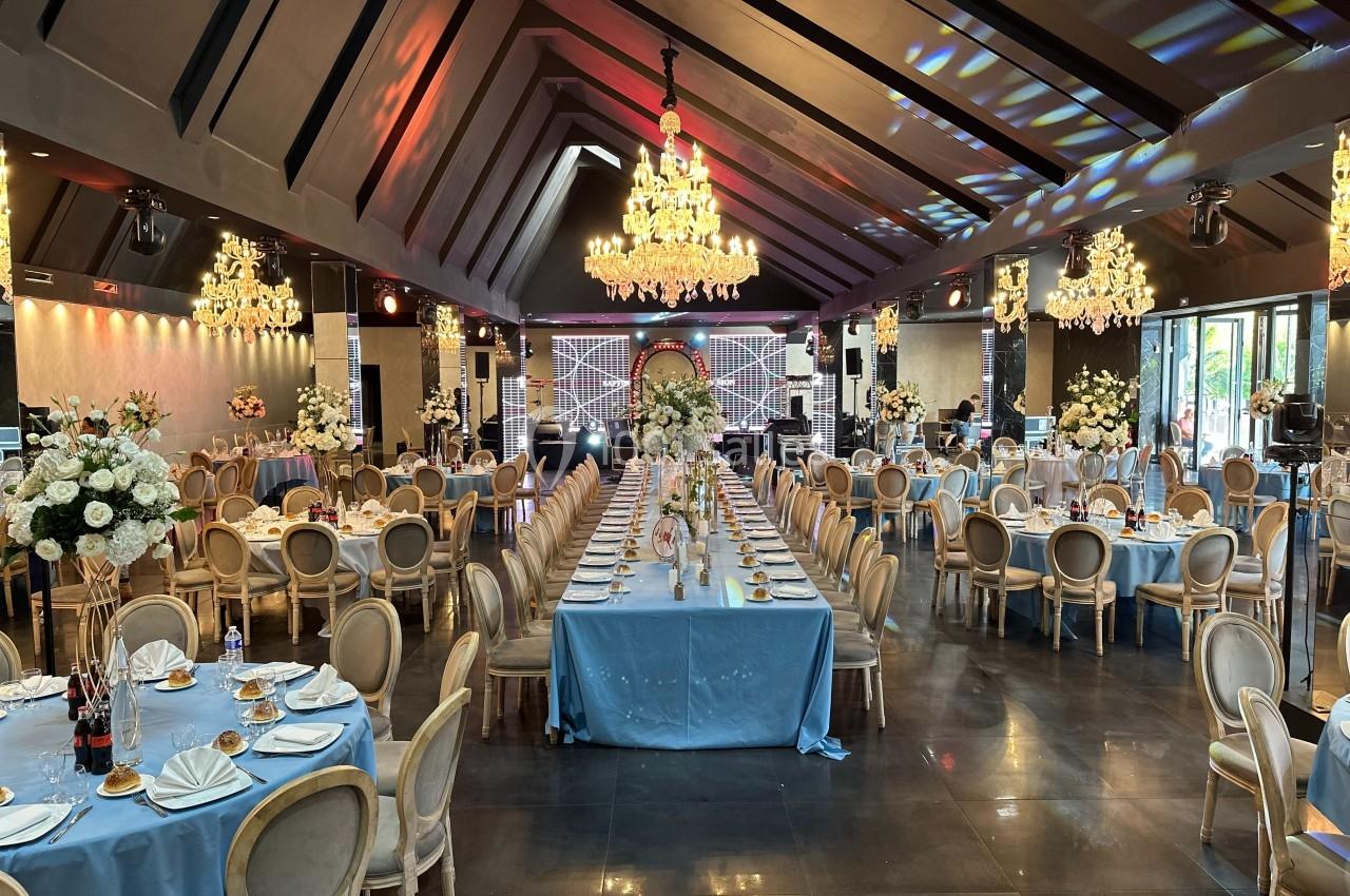Salle de réception élégante avec tables dressées, nappes bleues, chaises classiques et lustres imposants.