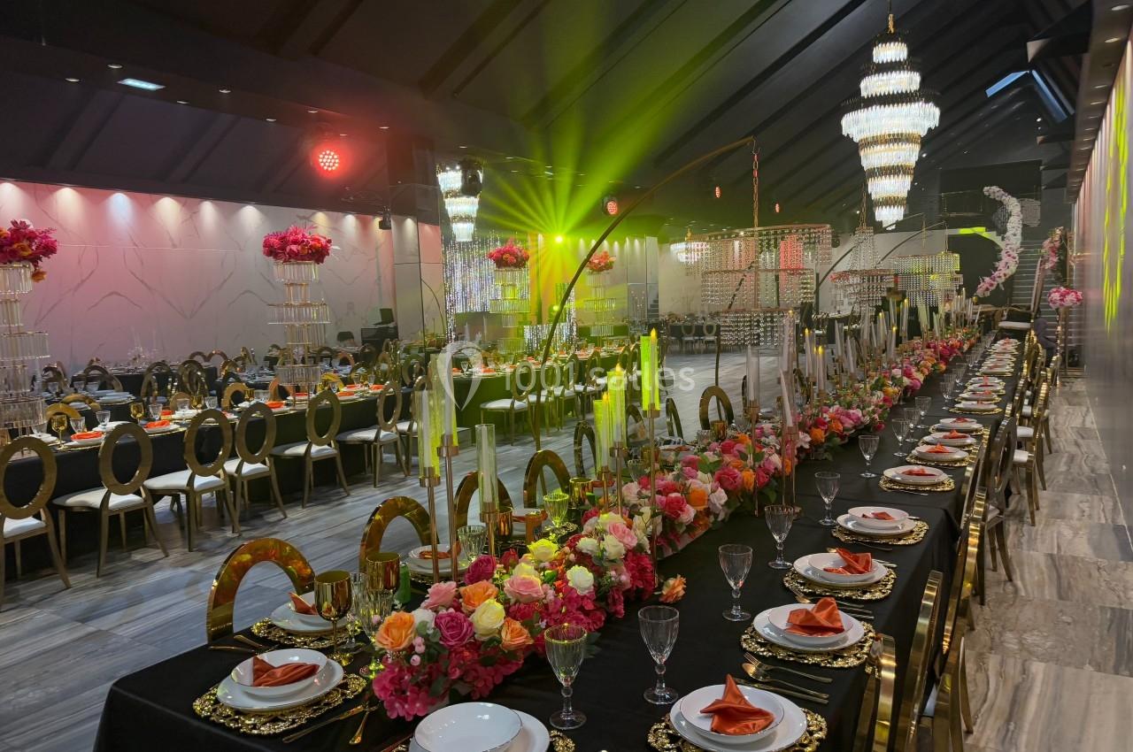 Salle de réception décorée avec des tables élégantes, des chandeliers imposants et des arrangements floraux colorés.