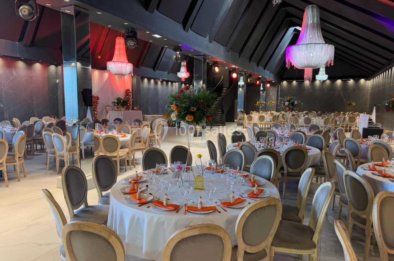 Salle de réception élégante avec tables rondes dressées, chaises en bois clair et lustres suspendus.