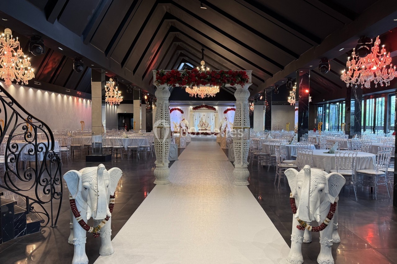 Salle de réception décorée avec une allée centrale bordée d'éléphants ornés et d'un arche fleuri, tables dressées en arrière…