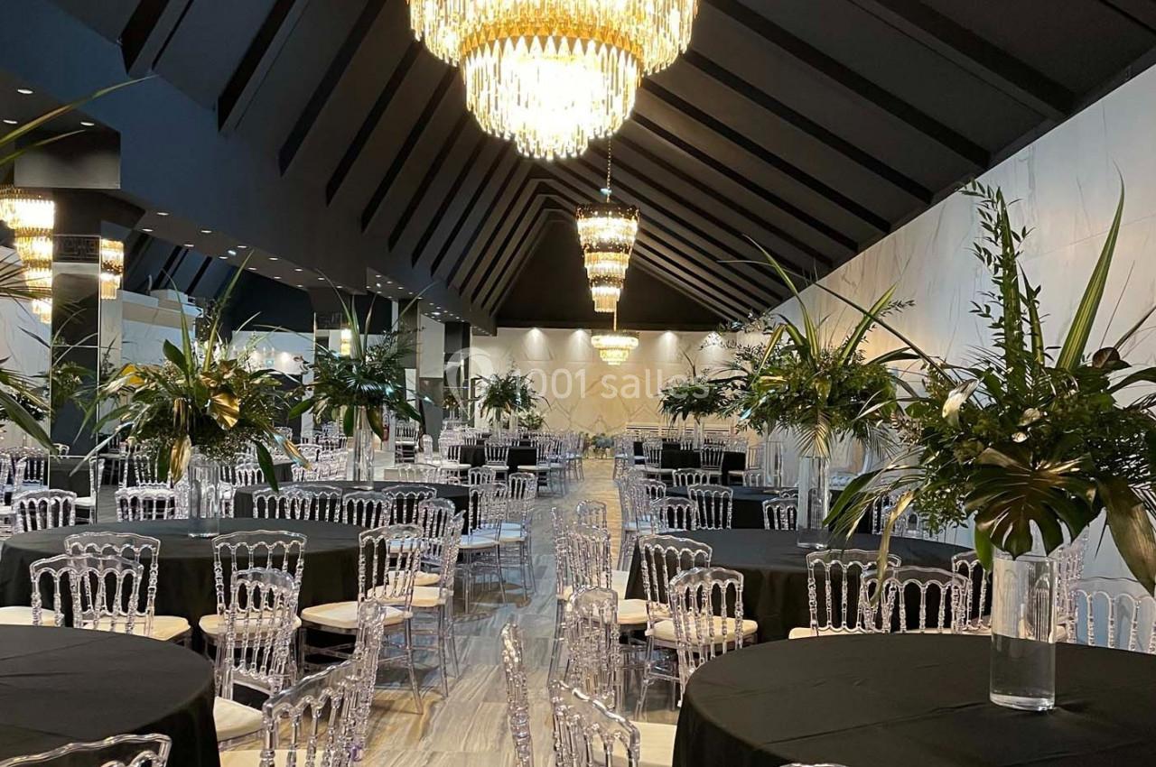 Salle de réception élégante avec tables rondes dressées, chaises transparentes et lustres suspendus.