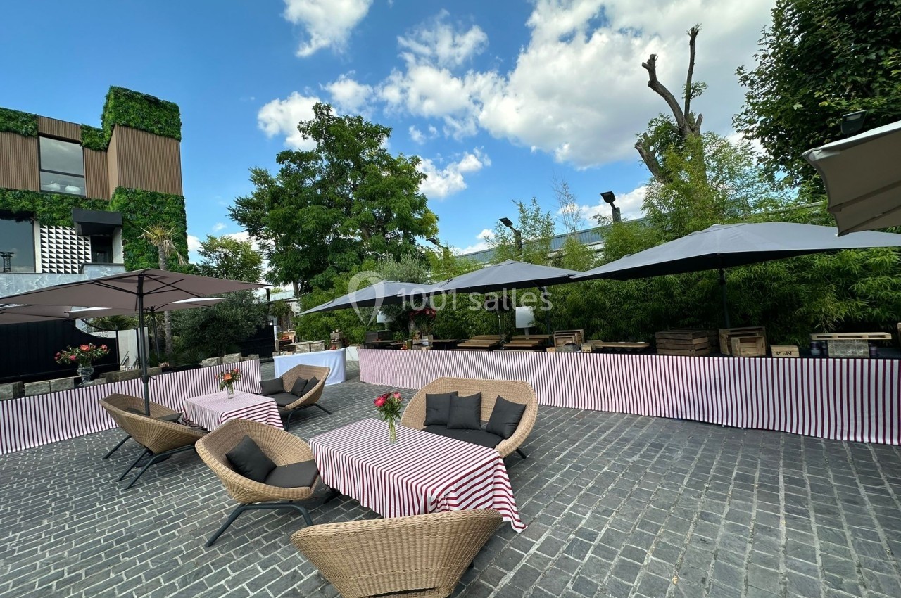 Terrasse extérieure avec tables et chaises en rotin, nappes rayées, parasols et végétation environnante.