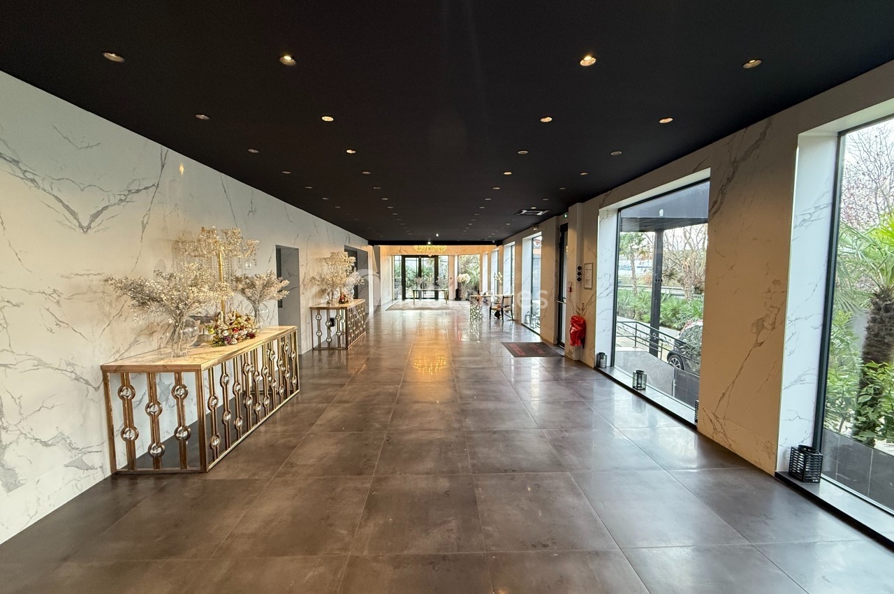 Hall spacieux avec sol en carrelage sombre, murs effet marbre, éclairage encastré et grandes baies vitrées donnant sur l…