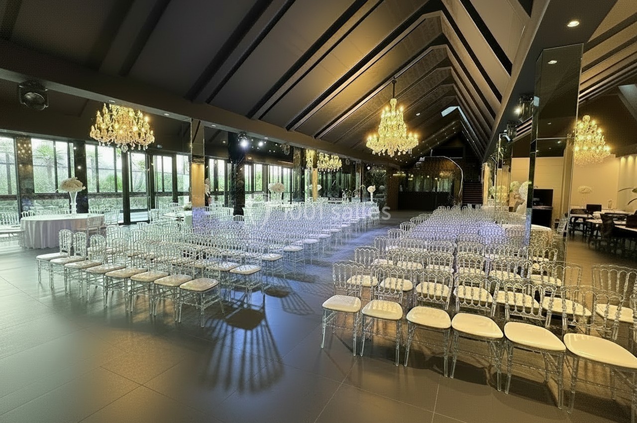 Salle de réception élégante avec rangées de chaises transparentes, lustres suspendus et grandes baies vitrées.