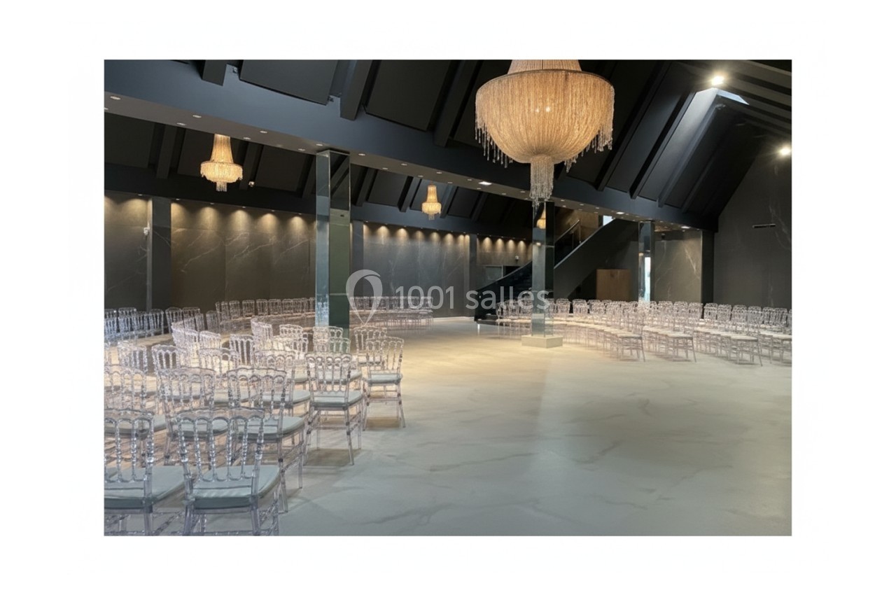 Salle spacieuse avec des chaises transparentes alignées, éclairée par des lustres suspendus et un éclairage tamisé.