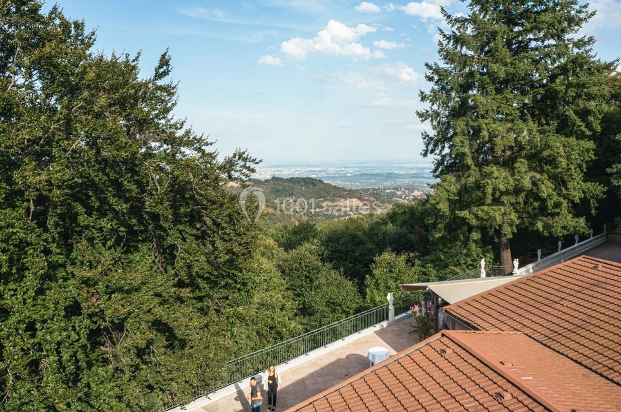 Vue sur un paysage vallonné avec des arbres, des toits en tuiles et une terrasse en premier plan.