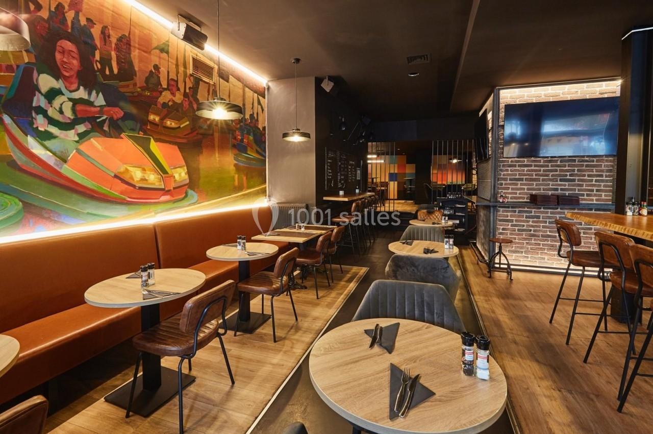 Salle de restaurant moderne avec tables en bois, chaises en cuir, fresque colorée et éclairage chaleureux.
