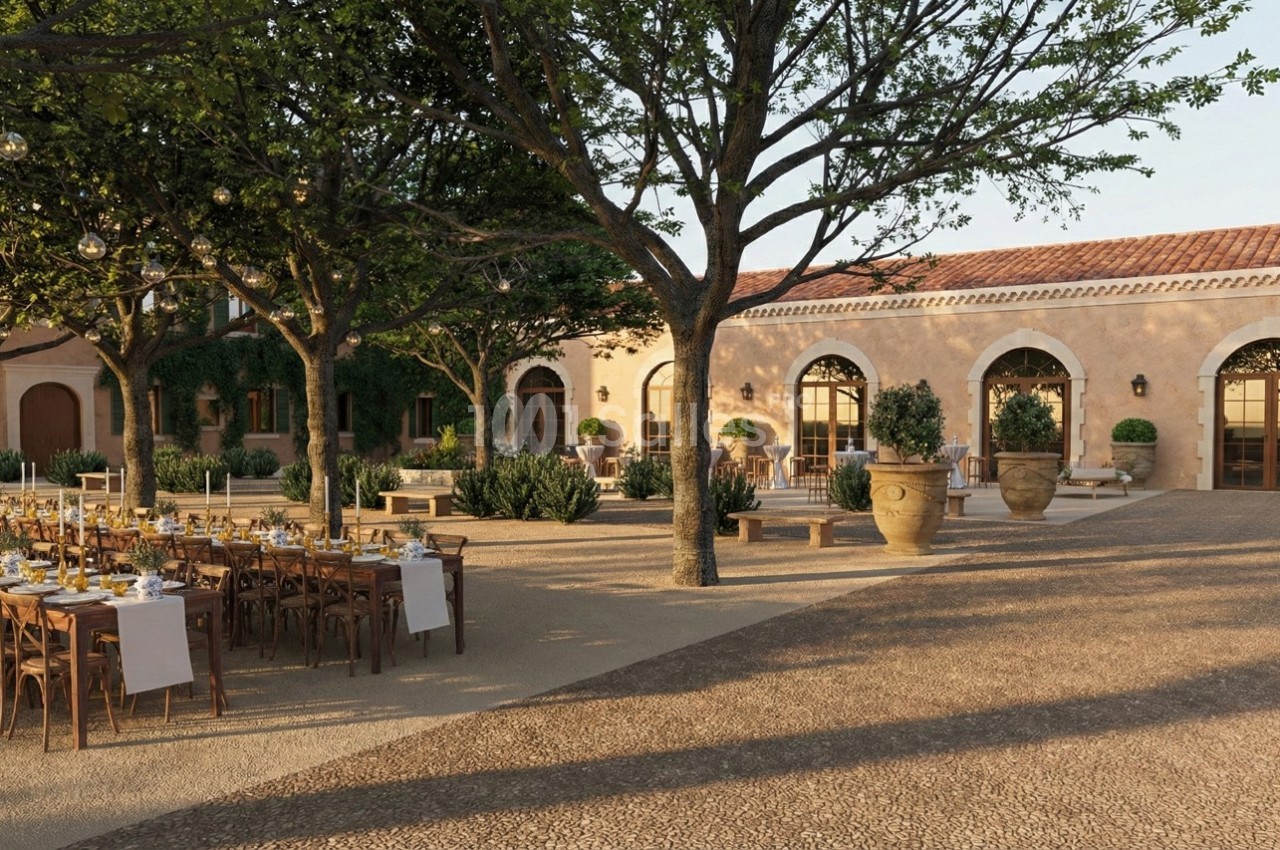 Cour extérieure aménagée avec des tables dressées pour un repas, entourée d'arbres et de bâtiments aux arches en pierre.